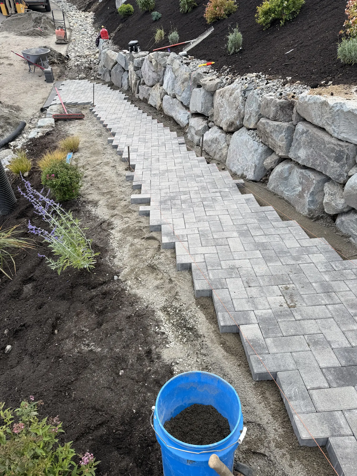 Paver walkway being laid beside a large stone retaining wall